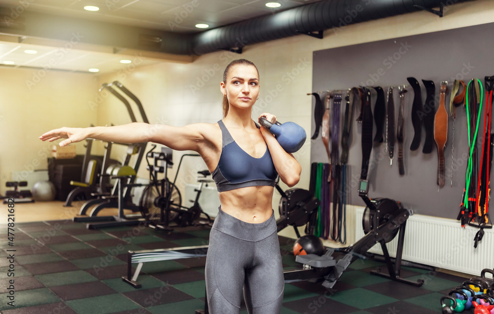 Wall mural Young muscular woman in sportswear trains with a kettlebell in the gym. Healthy lifestyle concept. Functional training