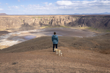 A lonely man with a dog standing on the edge of Al Wahbah crater (Makla Tamyah), Saudi Arabia - obrazy, fototapety, plakaty
