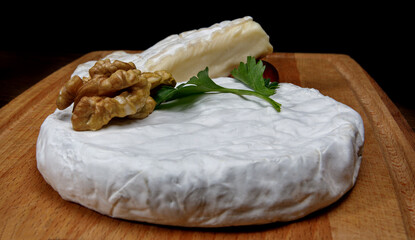 A circle of camembert cheese with white noble mold. A slice of walnut cheese.
