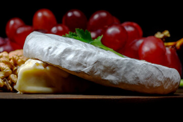 A circle of camembert walnut cheese and grapes lie on a wooden board.