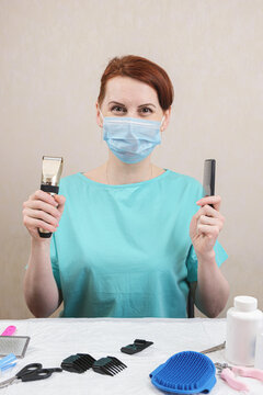 Vertical Portrait Of Female Groomer With Pet Grooming Tools. Specialist In Grooming Dogs And Cats. Woman In A Medical Mask Holds An Electric Pet Clipper And Hairbrush