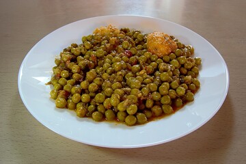 Green peas and potatoes cooked in a tomato sauce dish. Closeup view, shallow depth of field