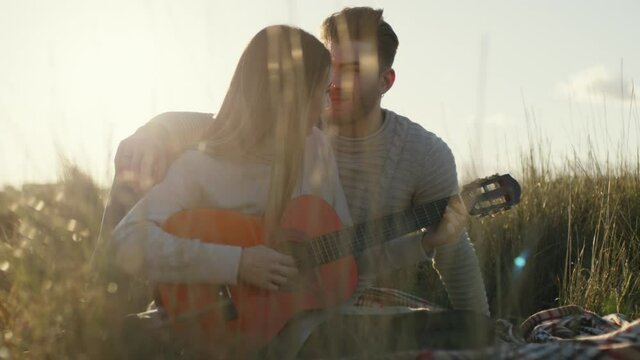Coppia ragazzo e ragazza suonano la chitarra seduti su un tappeto in campagna al tramonto per san valentino