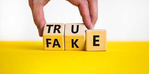Fake or true symbol. Businessman turns wooden cubes and changes the word fake to true or vice versa. Beautiful yellow table, white background, copy space. Business and fake or true concept.