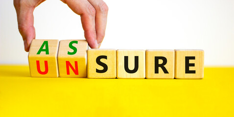Assure or unsure symbol. Businessman turns wooden cubes and changes the concept word unsure to assure. Beautiful yellow table, white background, copy space. Business and assure or unsure concept.