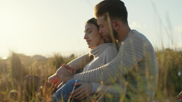 Coppia di ragazzo e ragazza si abbracciano da seduti in campagna vicino al mare al tramonto