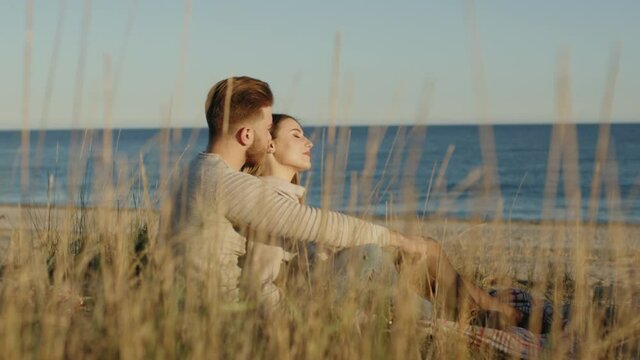 Coppia di ragazzo e ragazza si abbracciano da seduti in campagna vicino al mare al tramonto