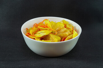 Pickled cabbage with curry and carrots in a plate on a black background