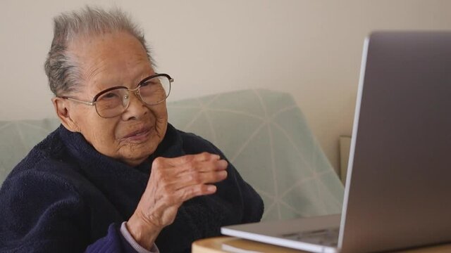 ノートパソコンと手を振るシニア女性