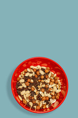 Cover page with different nuts and raisin collected at red plastic plate at turquoise green blue background with copy space, closeup, details. Concept healthy diet and nutritious food.