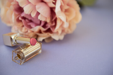 Obraz na płótnie Canvas Rouge à lèvres rose sur fond mauve avec fleur rose en arrière-plan - décor féminin