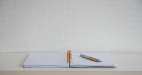Cahier à spirale ouvert sur une page blanche avec un stylo sur un bureau blanc pour trouver...