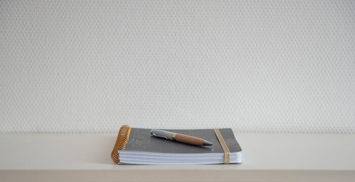 Cahier &agrave; spirale ferm&eacute; avec un stylo pos&eacute; dessus sur une &eacute;tag&egrave;re blanche et mur blanc - carnet simple et &eacute;pur&eacute;