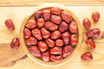 Several sweet dried ziziphus berries with a wooden tray on a wooden table, close-up, top view.