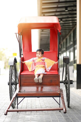 Asian cute little girl in Japanese traditional costume sitting on a rickshaw vintage style.