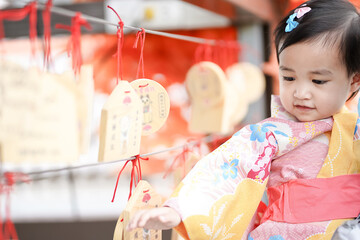 Asian cute little girl in Japanese traditional costume blessing a wish with hanging woods in a...
