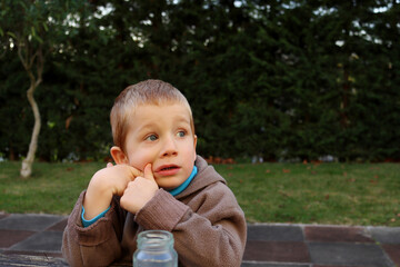 A blond boy dreamily looks into the distance, opening his mouth. A four-year-old boy props his cheek with his hand. 