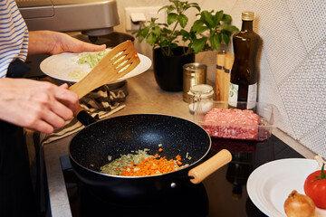 Woman cooking bolognese sauce in pan on induction stove in the kitchen