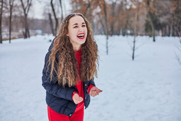 a young happy woman is having fun in a winter park, throwing snow, it is cold in her hands, the emissions are off scale.