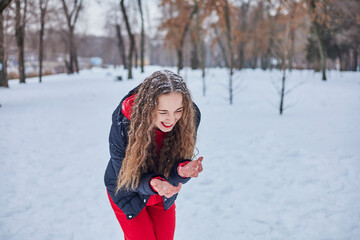 a young happy woman is having fun in a winter park, throwing snow, it is cold in her hands, the emissions are off scale.
