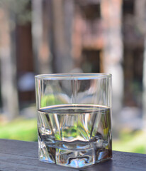 Glass shot with a transparent, colorless drink on a wooden table in a summer cafe. On a blurry, unfocused background