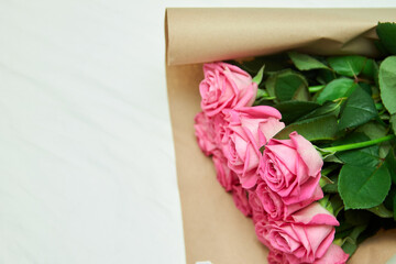 Pink roses in a package with green stems without thorns lie on a white bed. A nice gift from the hotel.