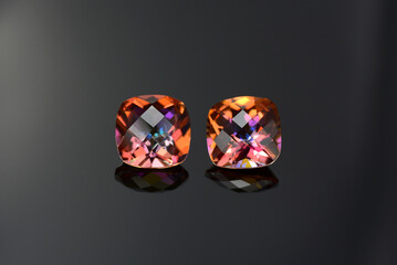 Fototapeta premium Azotic topaz gemstones matched pair. Square barrel shaped, checker faceted, multicolor rainbow, titanium coated, full of flashes, sparkles, transparent, semiprecious gem settings. Black background.