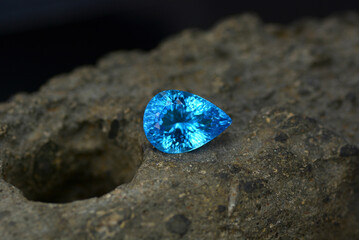 Millennium concave cut swiss blue topaz gemstone placed on an ancient Neolithic stone axe hammer. Black background. Textured free space. Gemology geology theme. Blue gem was heated treated irradiated