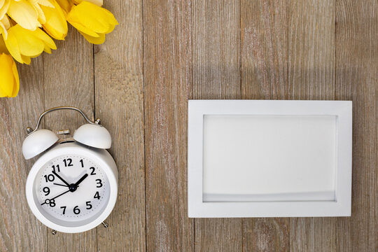 White alarm clock wooden board blank frame yellow tulips.  Background for Spring, Daylight Savings, Mother's Day, Easter, Reminder, Goals, Copy Space.
