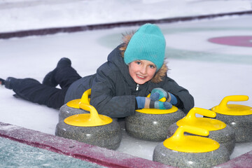 the child lies on the ice for the team winter curling sport, next to the rocks for the game