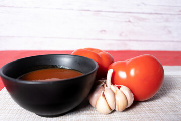Sauce prepared in a black pot and ingredients to prepare it (garlic and tomato)