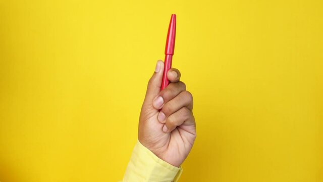 hand hols a red color pen against yellow background 