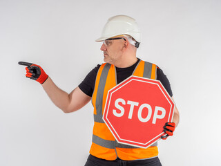 Stop road sign. Builder warns of danger. Worker indicates direction. Road hazard warning. Concept is prevention of accidents. Stop warning. Mature man in uniform of construction worker.