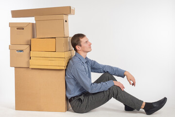 A man with many boxes. Boxes symbolize change of residence. Man is tired of moving to new home. Guy with boxes on white background. Guy is thinking about logistics of personal belongings