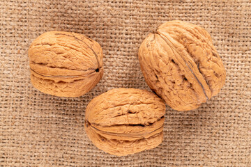 Three organic walnuts on burlap, close-up, top view.