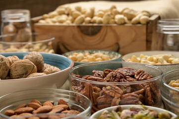 Different nuts and bowls closeup on a wooden table and brown background. Peanut, nut, cashew, almond, hazelnut, pistachio