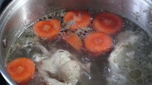 Chicken and bright orange carrot broth is cooked in a steel saucepan.