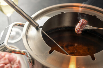 Crispy fried piece of meat on a long fork over a fondue pot with hot oil, convivial dinner often served at New Year for friends and family, selected focus