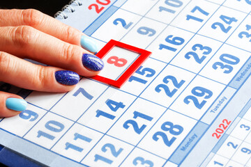 A woman's hand with a manicure points to the calendar with the date of the international women's holiday March 8 highlighted in red