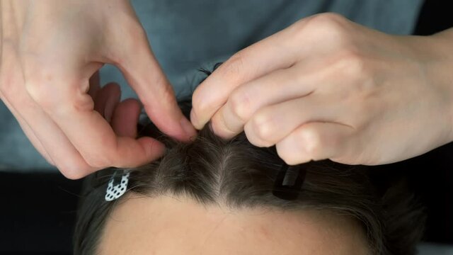 Woman is doing french braid on short men's hair, closeup view. She is doing a man's hair while sitting at home on the couch. Evening of a young married couple together.