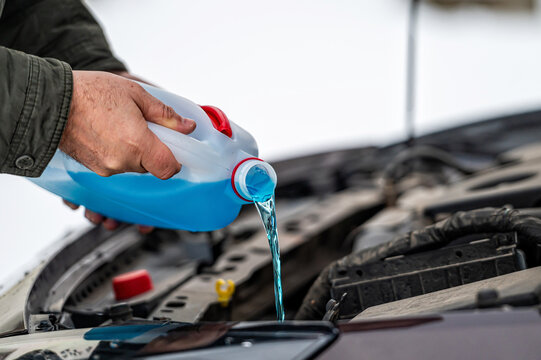 driver refilling the blue non-freezing windshield washer liquid in the tank of the car, close-up