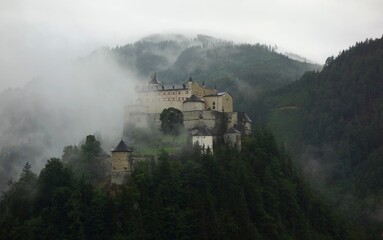 Fototapeta premium Old castle in the forest between mountains partly covered with fog 