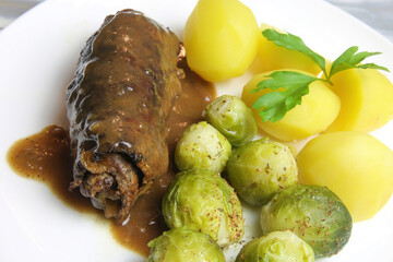 Closeup of isolated white plate with fresh homemade typical german beef roulades, brown sauce, cooked potatoes and green brussels sprouts
