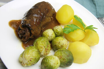 Closeup of isolated white plate with fresh homemade typical german beef roulades, brown sauce, cooked potatoes and green brussels sprouts