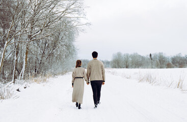 Young couple wearing knitted sweaters and walking along rural countryside path road in beautiful calm snowy winter day.