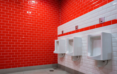 Row of 3 urinals on red and white tiles wall inside of men's toilet in modern style