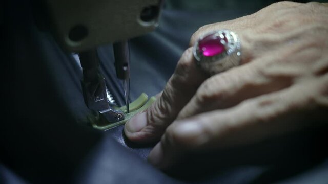 Close-up of old hands with silver ring of sewing master who makes complicated seam on black leather jacket next to the zipper. Tailor creates leather goods, stitches line along zipper. Slow motion.