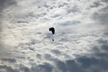 Contours of a paraglider with tourists in the back light in cloudy weather while flying through the sky.