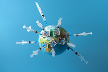   A globe on a blue background with many vaccination certificates on the needles of syringes. Copy...