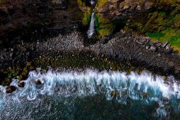 Long exposure aerial view of waves crashing in front of a coastal waterfall located on the south...
